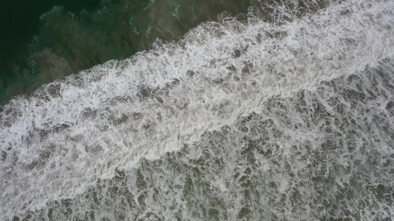 Wide whitewater pattern over shallow coastal water.