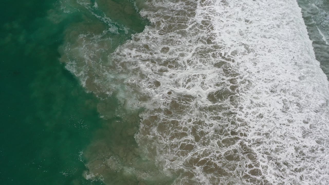 Dense white surf foam covers the right side of an overhead ocean frame.