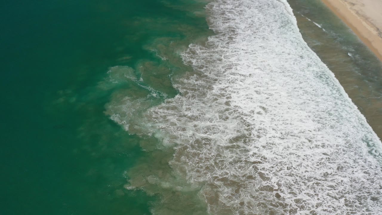 Green ocean water and white surf beside a sandy beach.