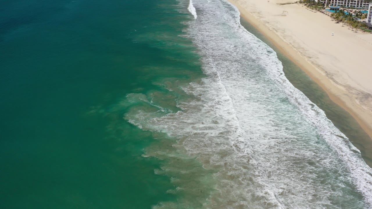 Aerial view of teal ocean waves breaking along a sandy beach.
