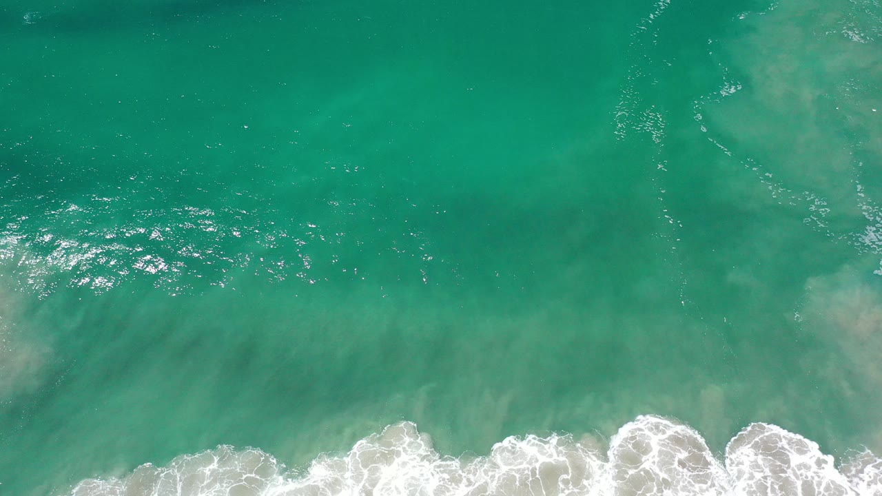 Overhead view of green-blue water and white surf along the lower frame in Los Cabos, Mexico, with no visible people.
