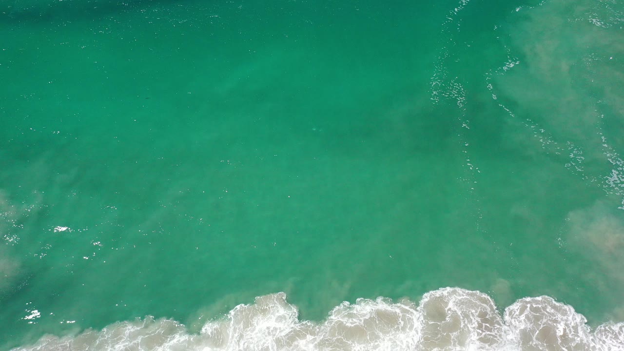 Overhead view of clear green sea in Los Cabos with white surf breaking along the lower edge and no visible people.