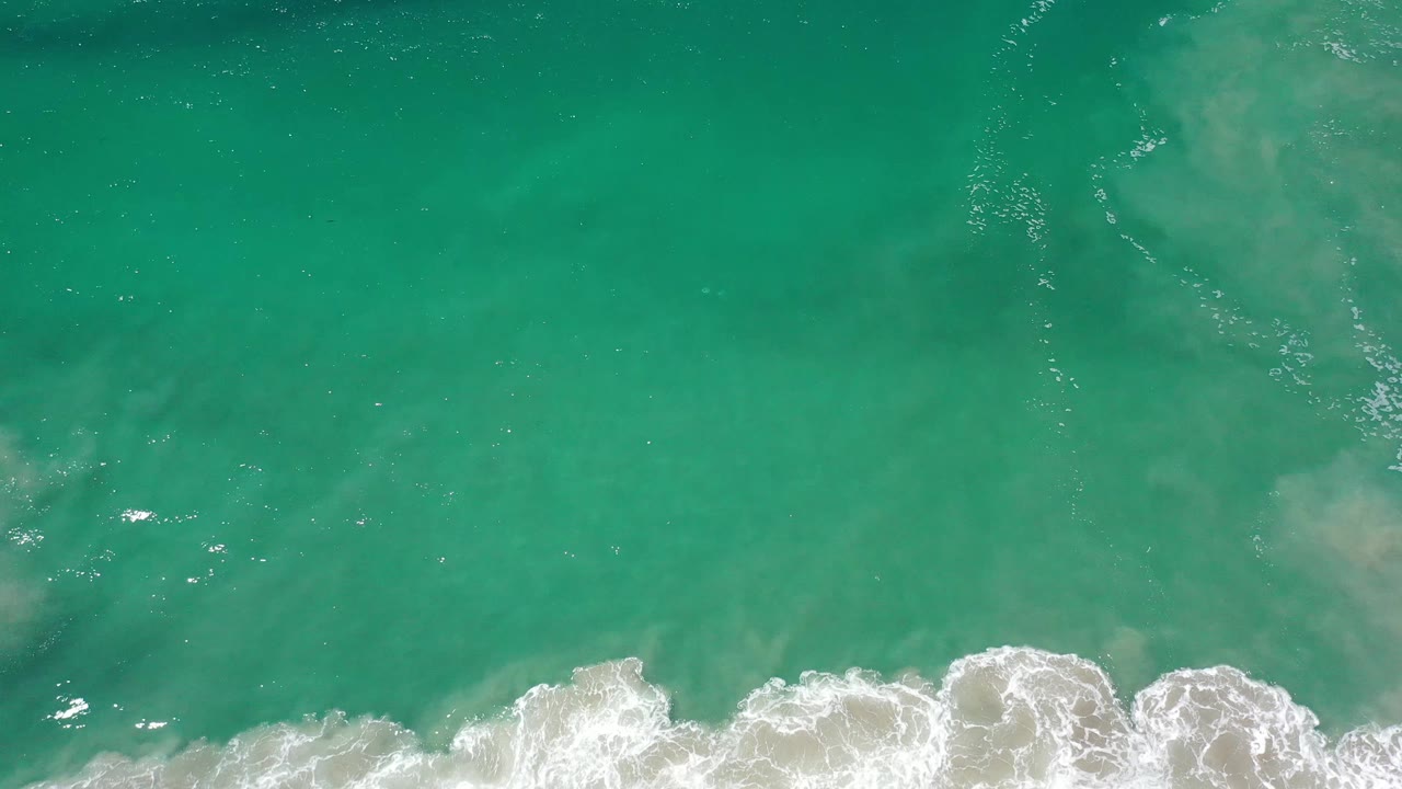 Clear green Los Cabos water fills the frame as a band of white surf foam curls across the bottom, with no visible people.