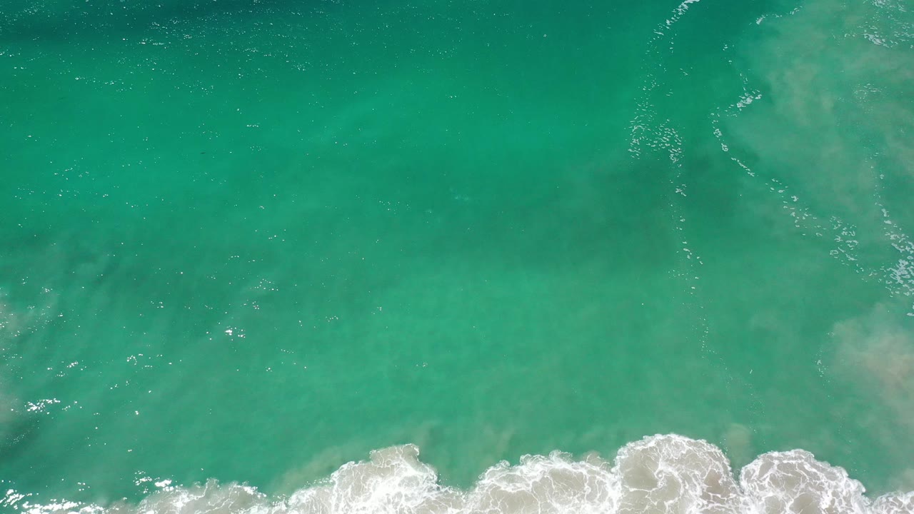 Sunlit green sea with pale underwater patches and surf below.