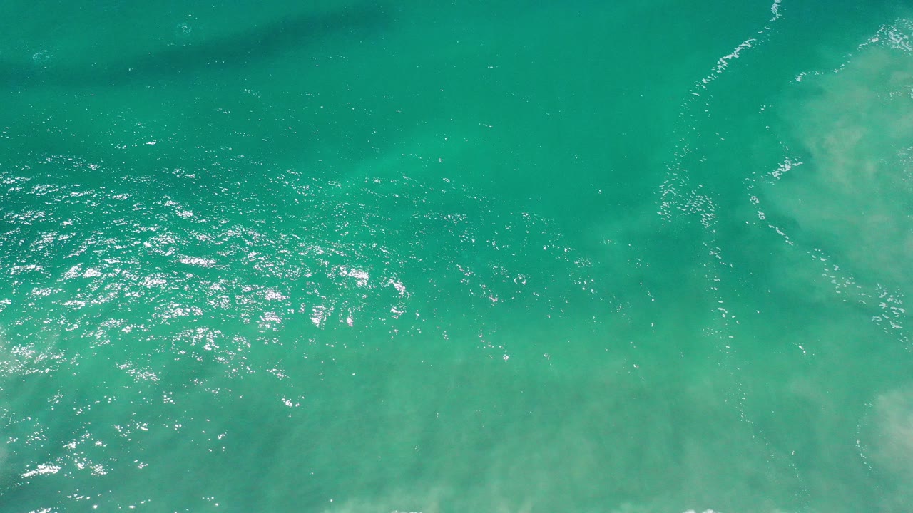 Opening overhead view of green sea water in Los Cabos, Mexico, with bright surface glare at left and pale underwater clouding, no visible people.