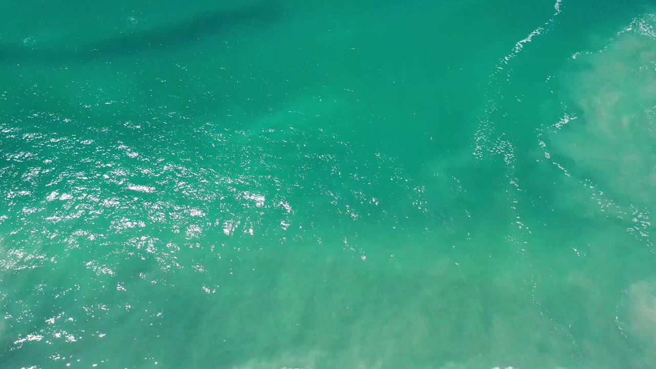 Overhead Los Cabos sea water with a pale submerged patch near the upper center and fine white ripples crossing the green surface, no visible people.