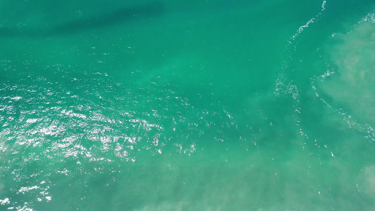 Aerial green sea surface with bright reflections and faint white ripple lines.