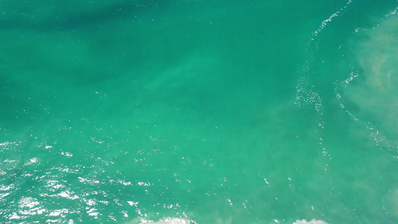 Overhead view of teal water in Los Cabos, Mexico, with small ripples, bright surface highlights, and no visible people.