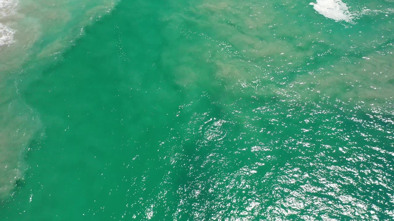 Aerial ocean water with a large darker green area and scattered white sparkle across the surface.