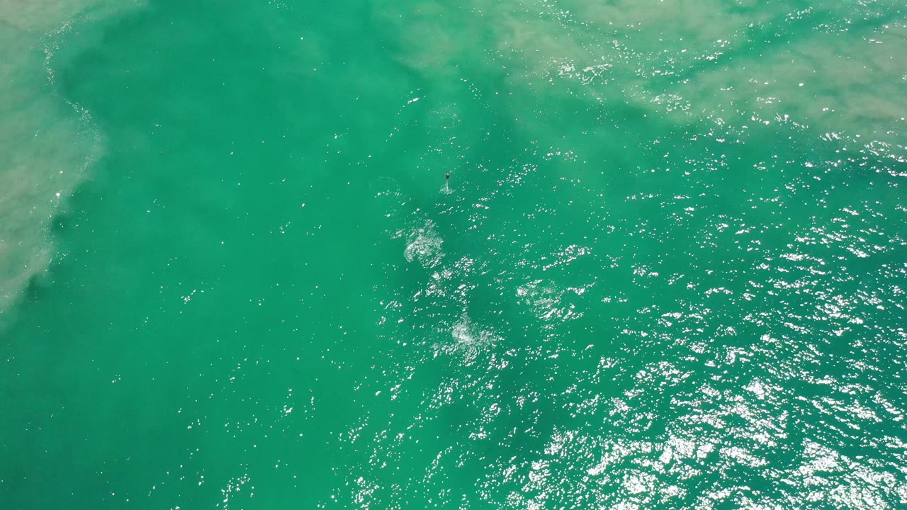Turquoise sea surface with ripples and pale clouding near the upper edge.