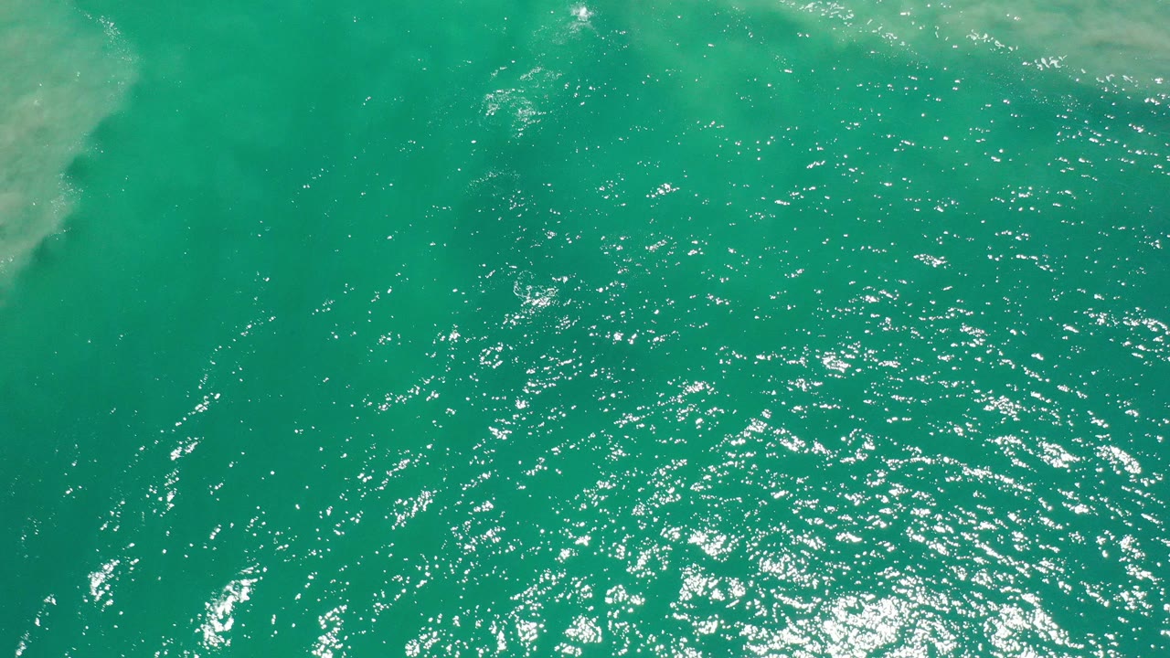 Overhead green water with sun glitter and faint pale patches.