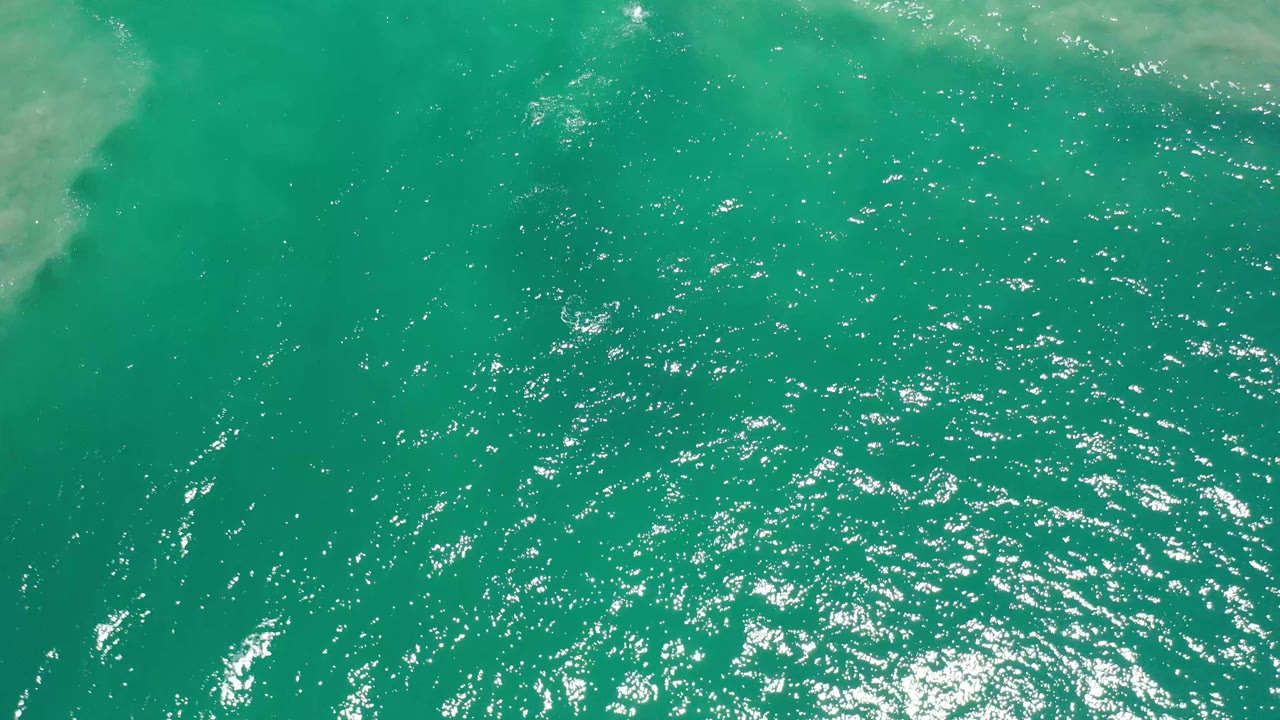 Top-down Los Cabos water view with green color, dense small ripples, a bright reflection cluster near the lower center, and no visible people.