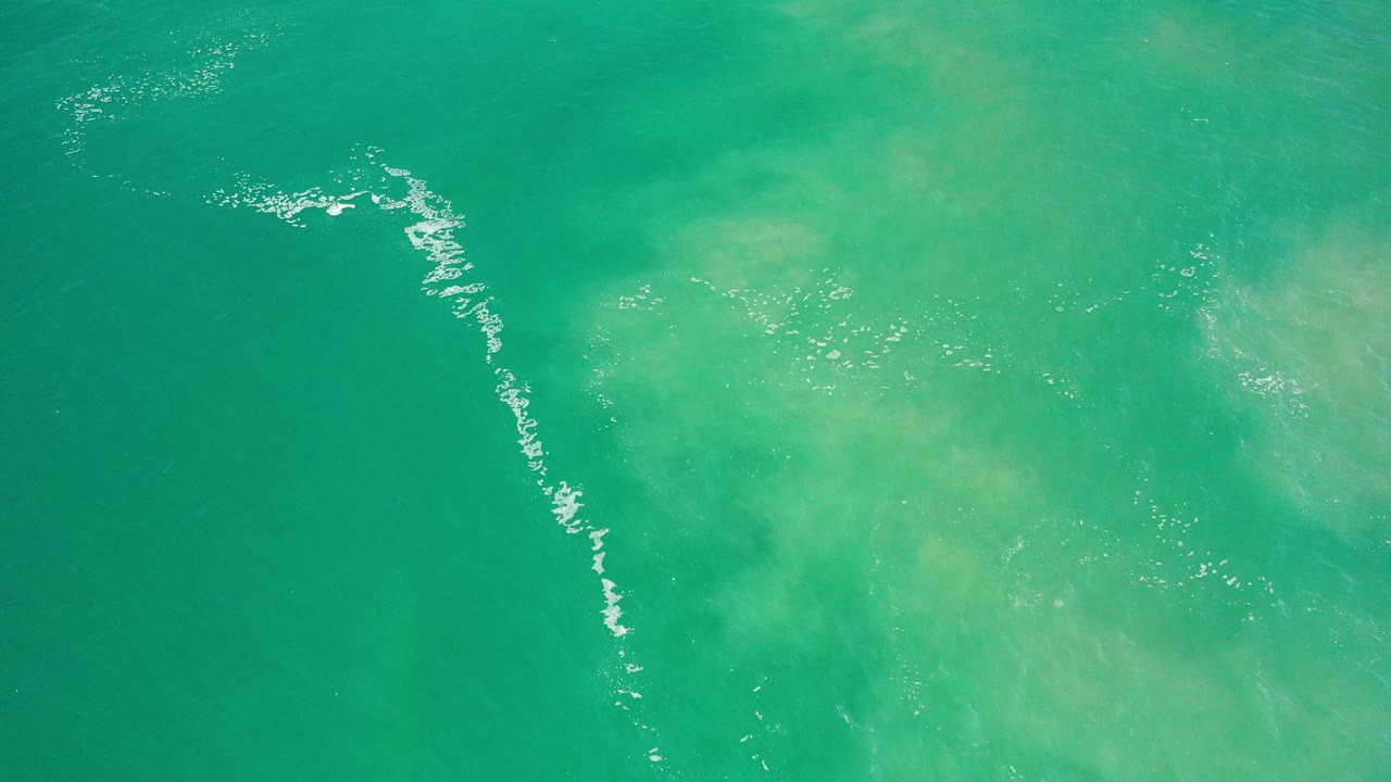 Top-down green sea water with a diagonal white foam line.
