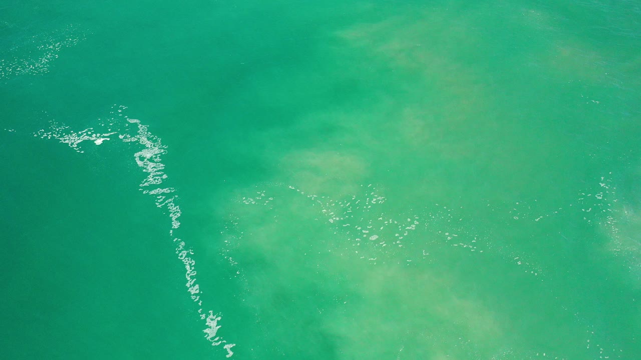 Turquoise ocean water seen from above with white ripples at left.
