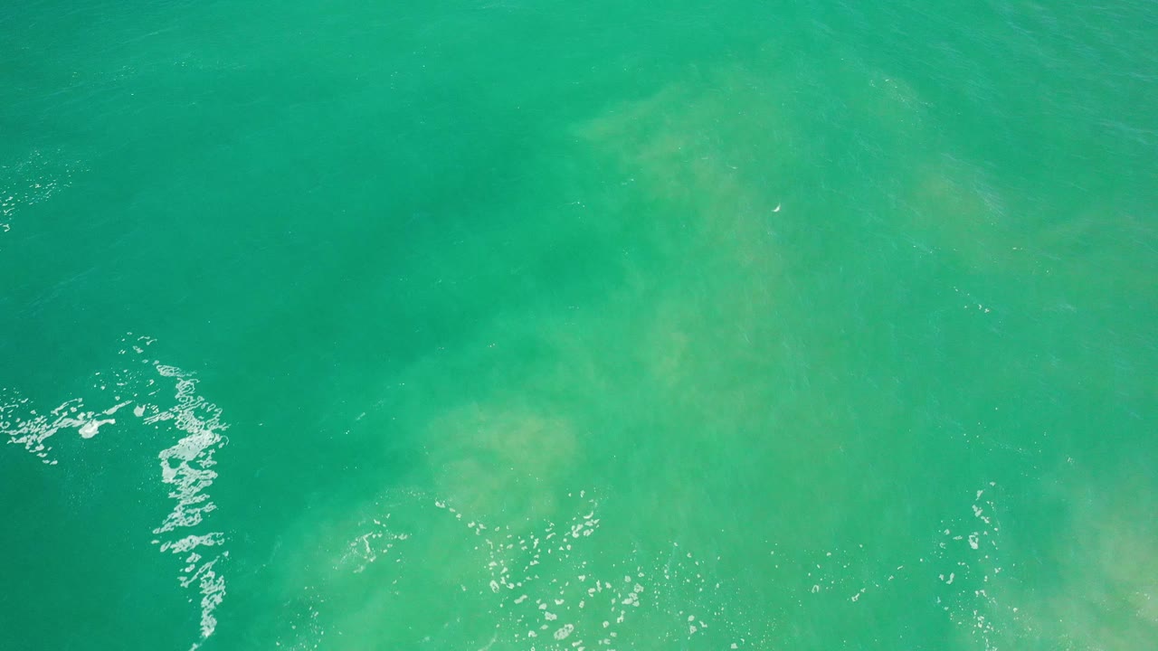 Turquoise ocean seen from above with a curved streak of white foam.