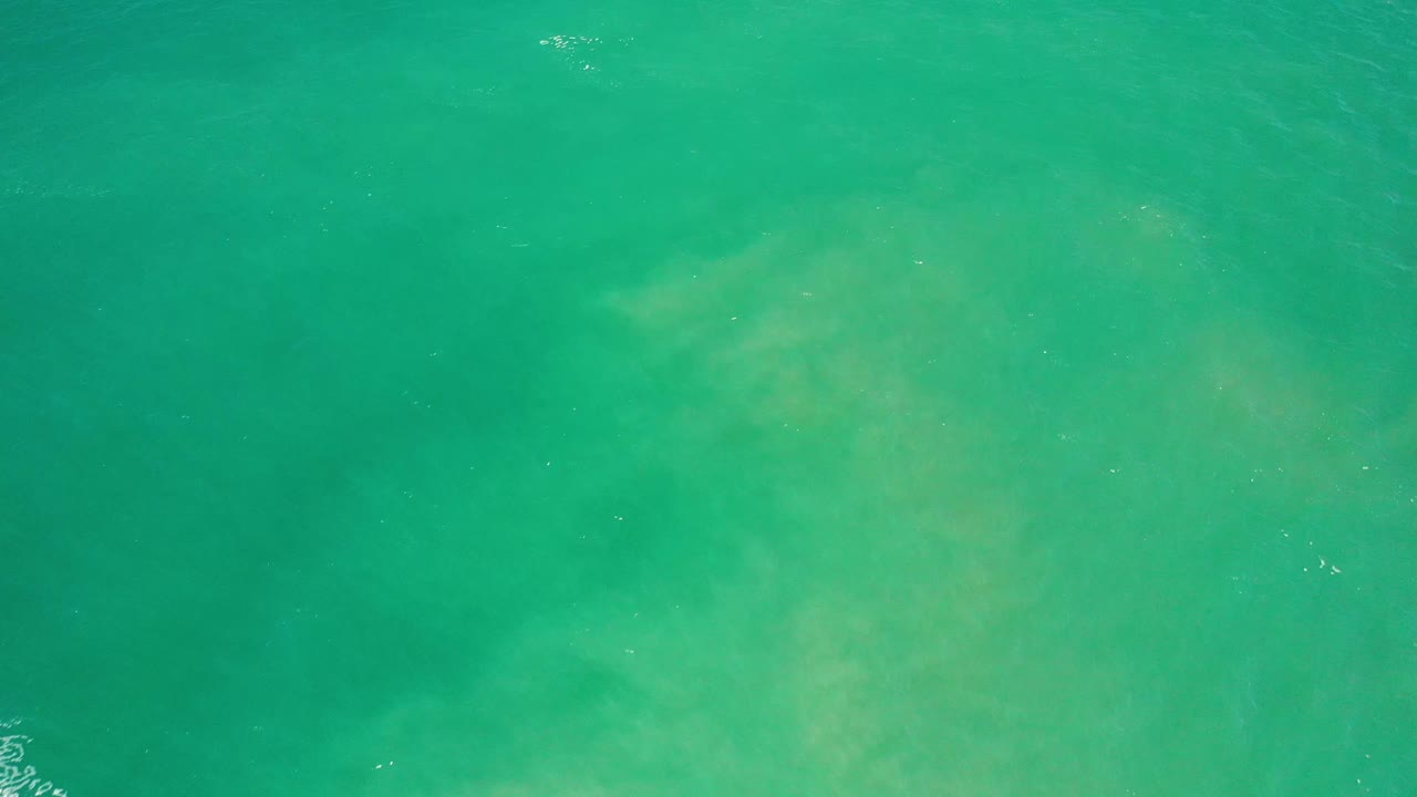 Green ocean surface in Los Cabos, Mexico, with soft lighter patches under the water and no visible people.