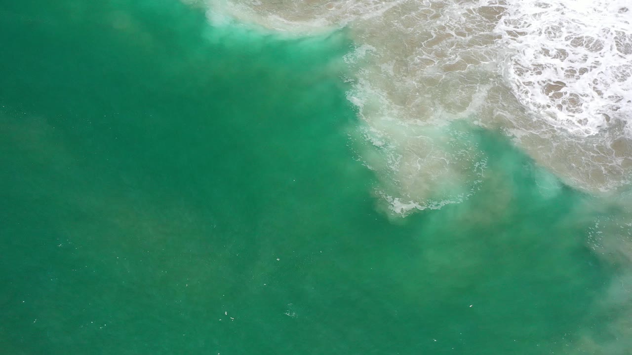 Aerial green water with white breaker foam and sand-colored shallows