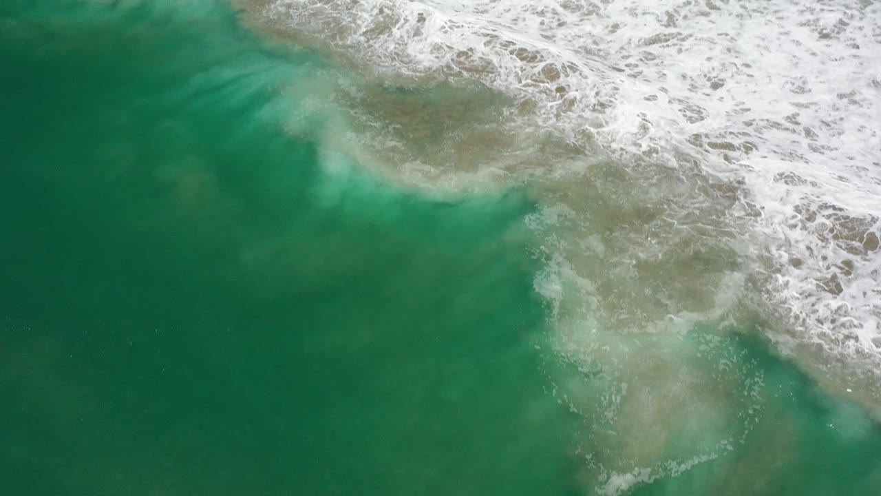 Overhead view of green ocean water in Los Cabos, Mexico, with white foam breaking across the upper edge and no visible people.