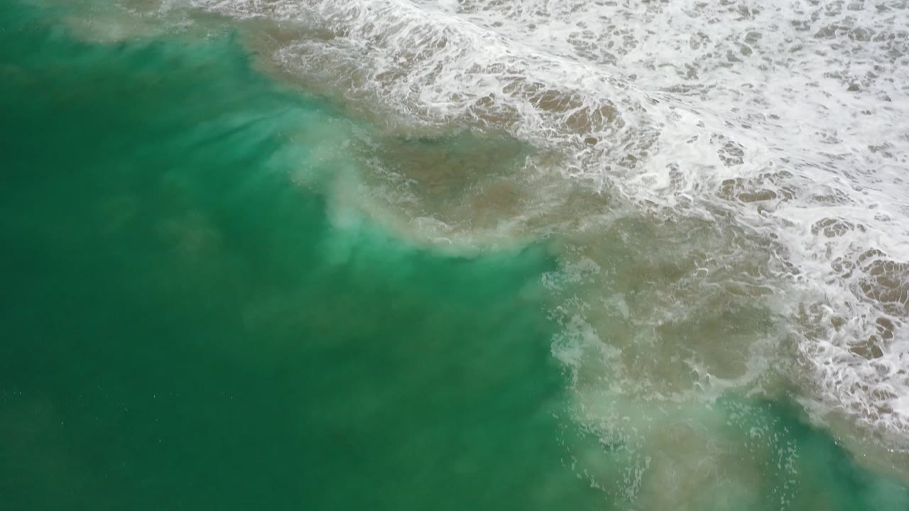 White surf spreads over shallow green and tan water.