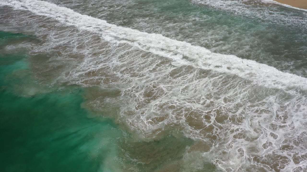 Overhead surf breaking across green shallow water.