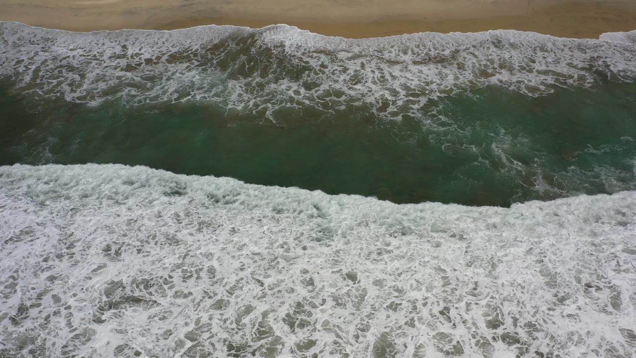 Overhead surf breaking toward a sandy beach.