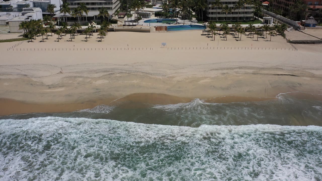Wide sandy shoreline with foamy water and hotels above the beach