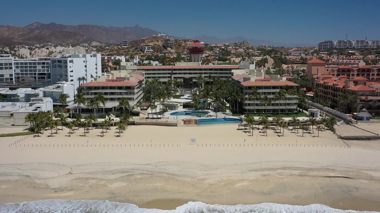 Beach resort frontage and surf below a dry mountain backdrop.