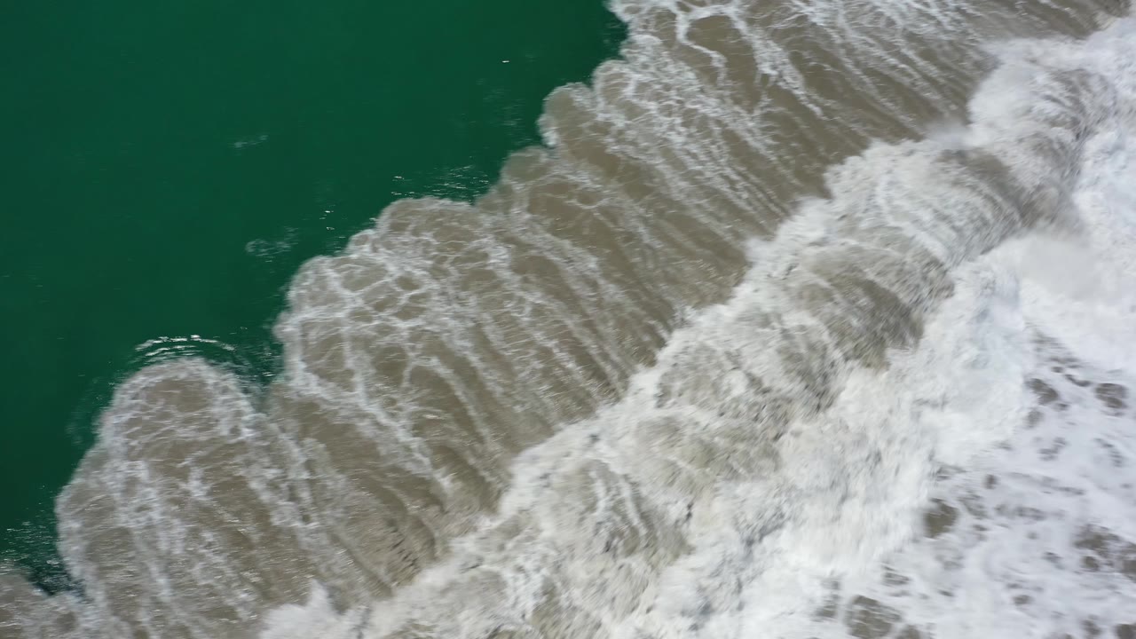 Foamy wave breaking across tan water.