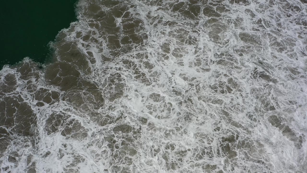 Overhead surf with white foam moving across dark water.