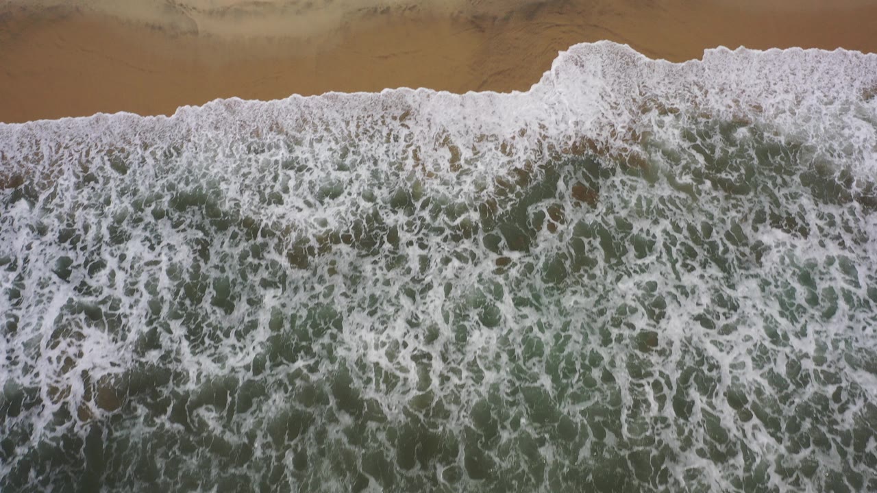 Overhead surf foaming across a sandy beach.