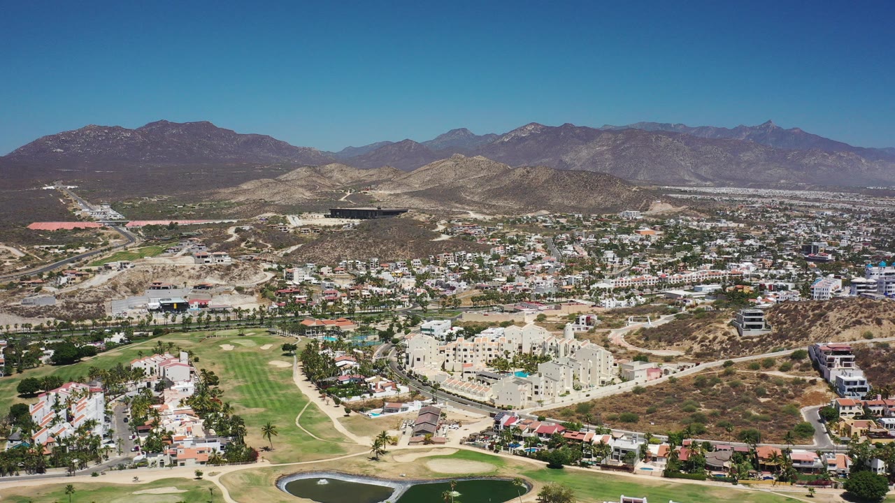 Aerial view of a Mexican town, golf course, dry hills, and mountains.