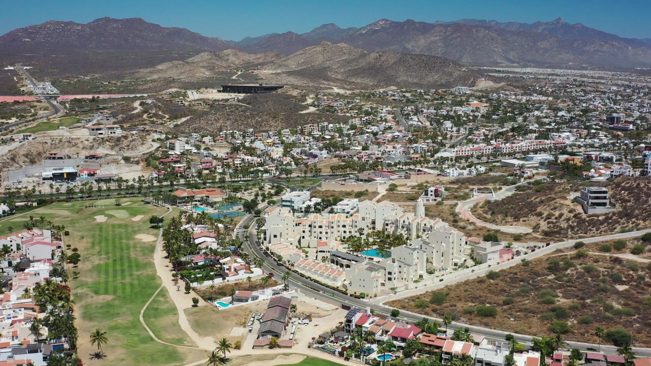 Aerial view of low-rise city, golf course, dry hills, and mountains.