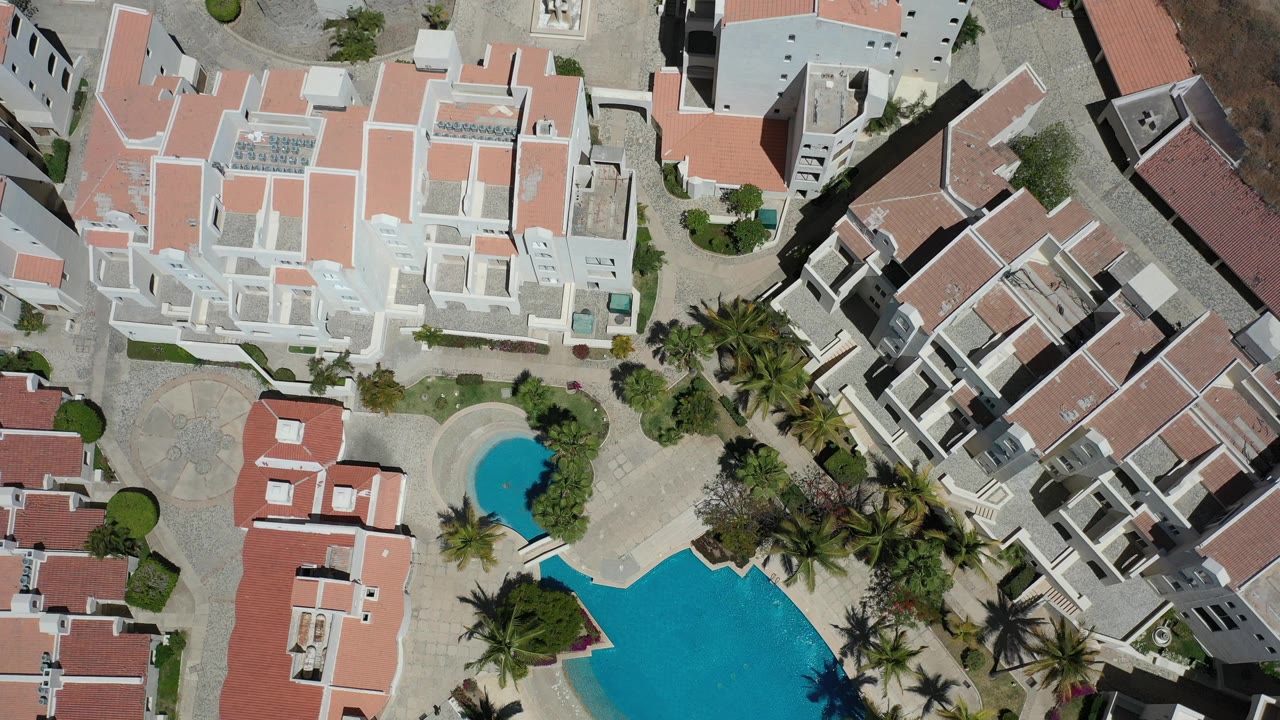 Top-down residential complex with red roofs and swimming pools.