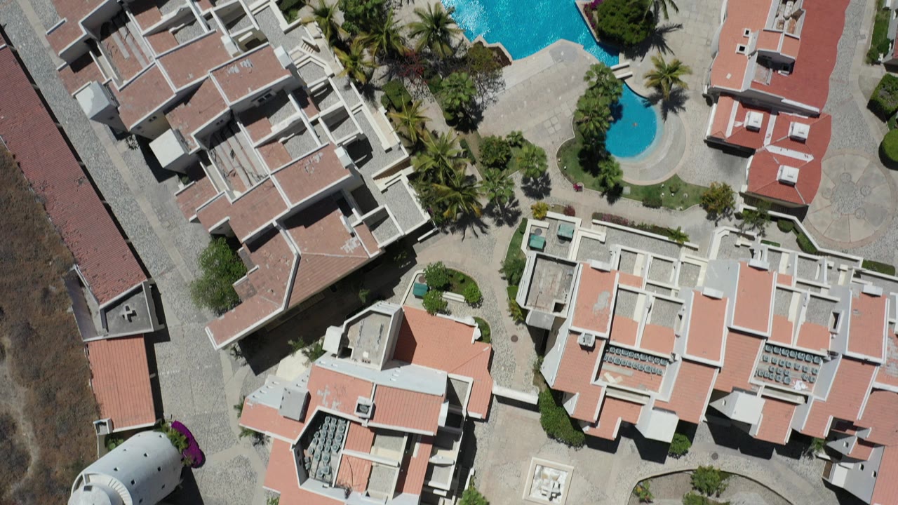 Overhead view of modern buildings, pools, palms, and paved resort grounds.