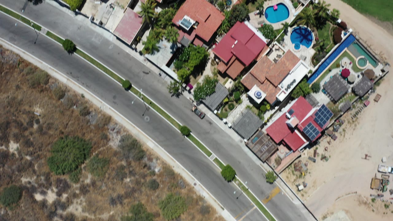 Overhead view of houses, pools, road, and dry land.