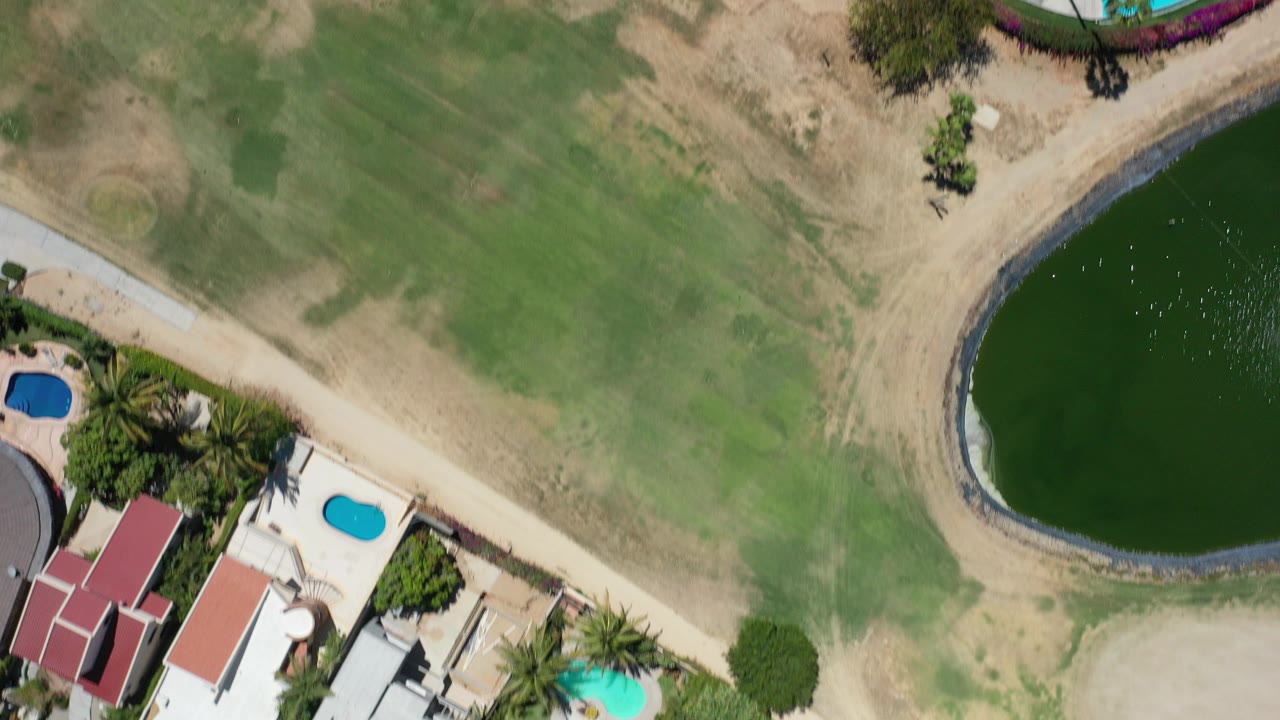 Overhead resort grounds with green field, curved pond, red roofs, and pools.