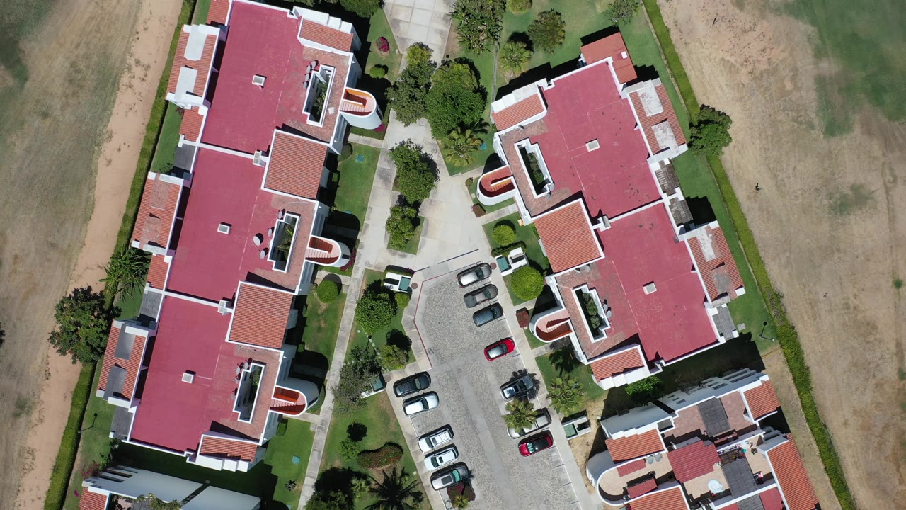 Overhead view of red-roofed buildings beside a parking area and dry ground.