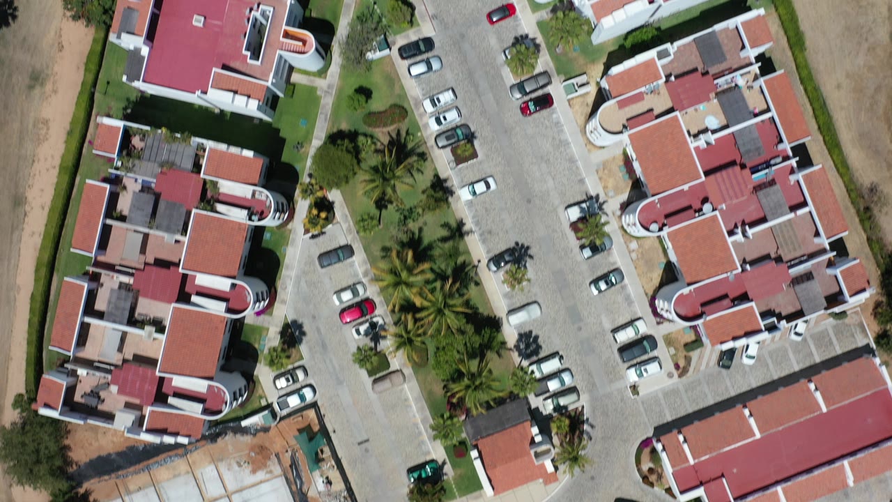 Overhead view of red-roofed hotel buildings beside parking and dry ground.