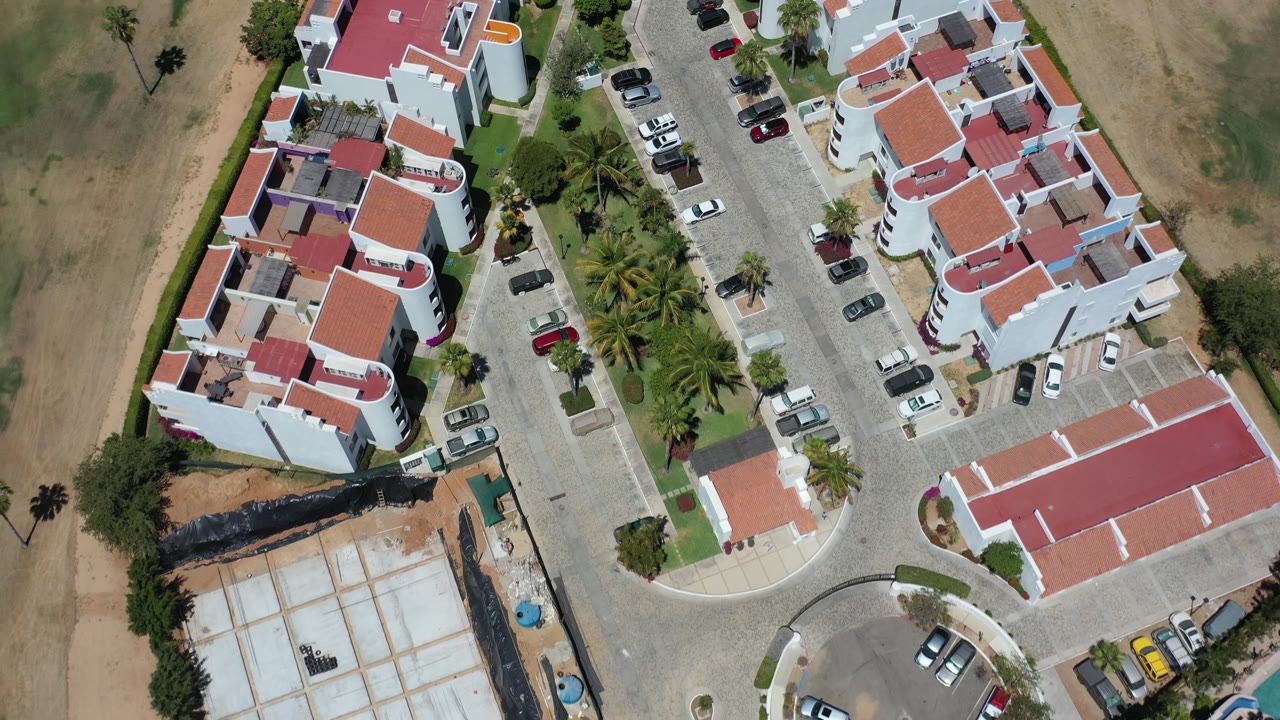 Top-down view of a residential block with a construction area and parked cars near dry land.