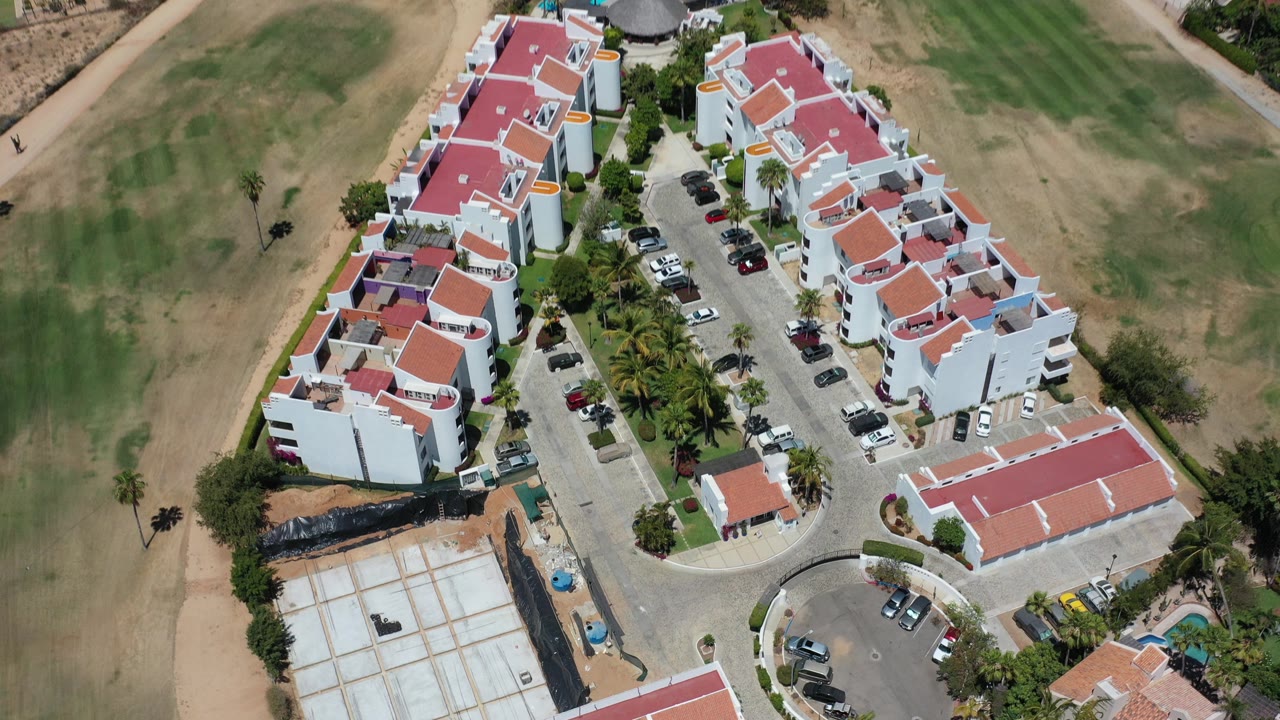 Aerial view of red-roof vacation homes beside dry golf-course grass.