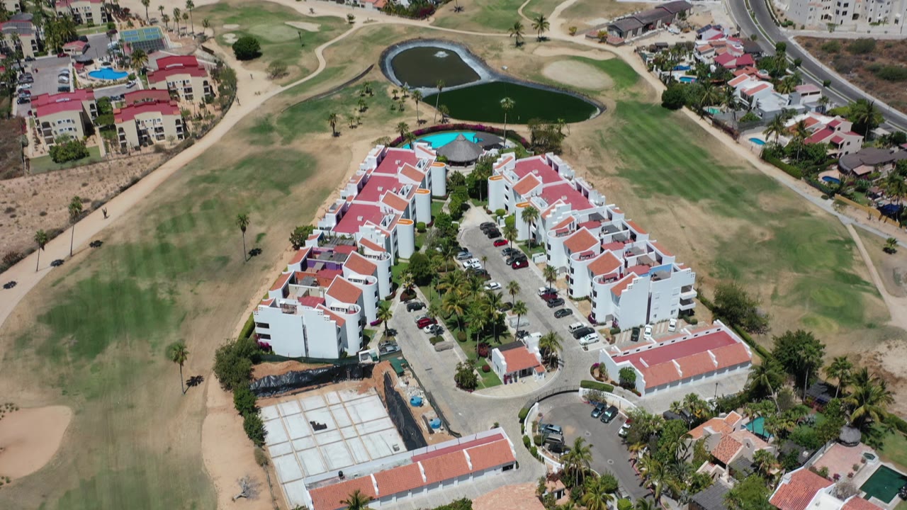 High aerial view of red-roofed buildings beside a golf course and ponds.