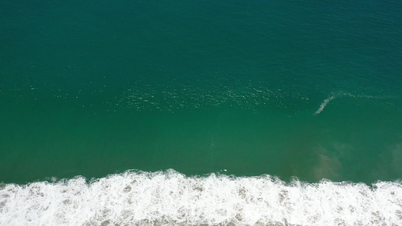 Top-down ocean water with white foam rolling across the bottom edge.