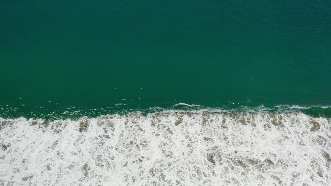 White wave break crossing a band of green coastal water.