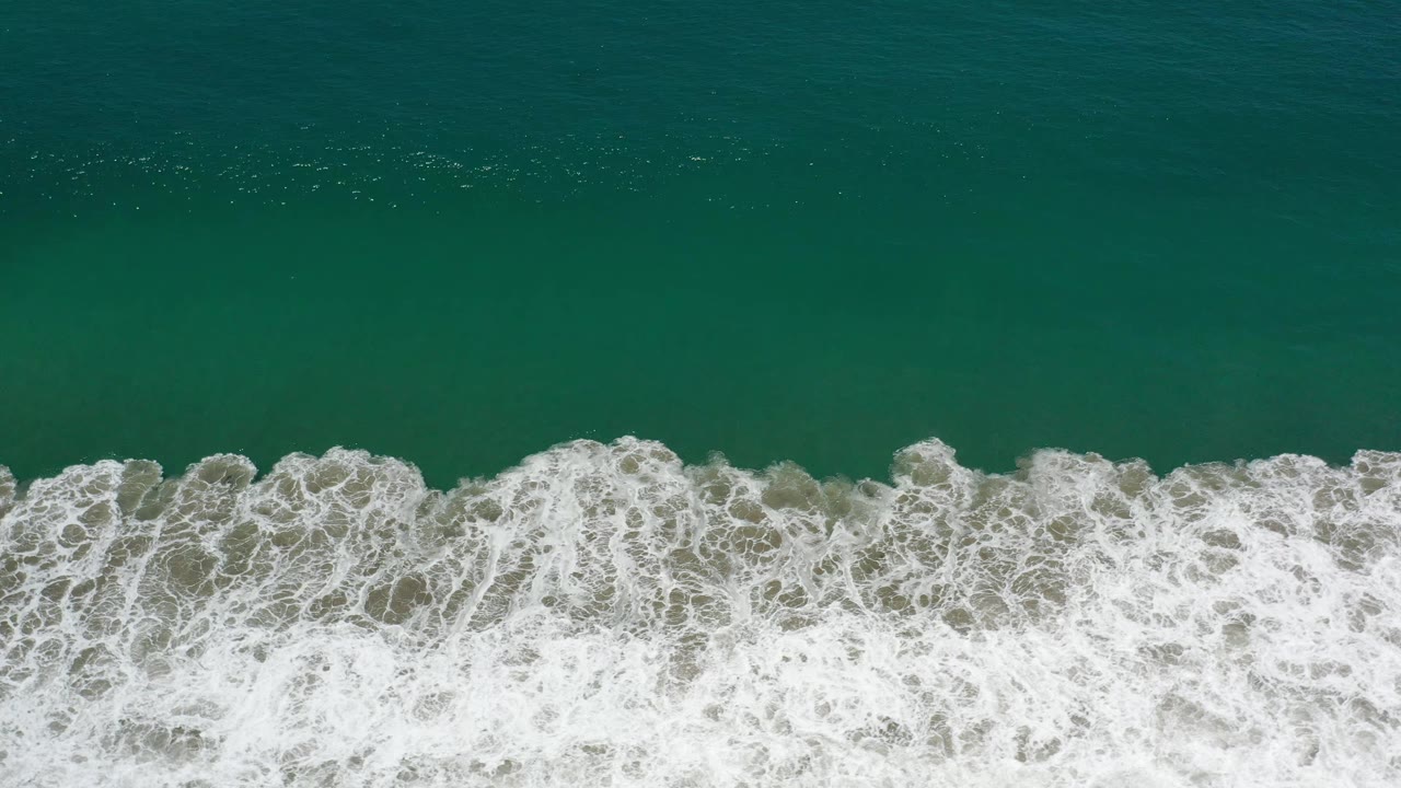 Aerial view of white foam spreading across green coastal water in Los Cabos, Mexico, with no visible people.