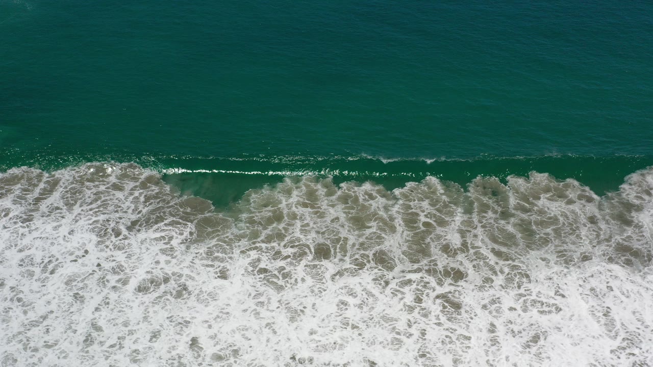 Overhead view of green ocean surf in Los Cabos, Mexico, with a broad band of white foam crossing the lower half and no visible people.
