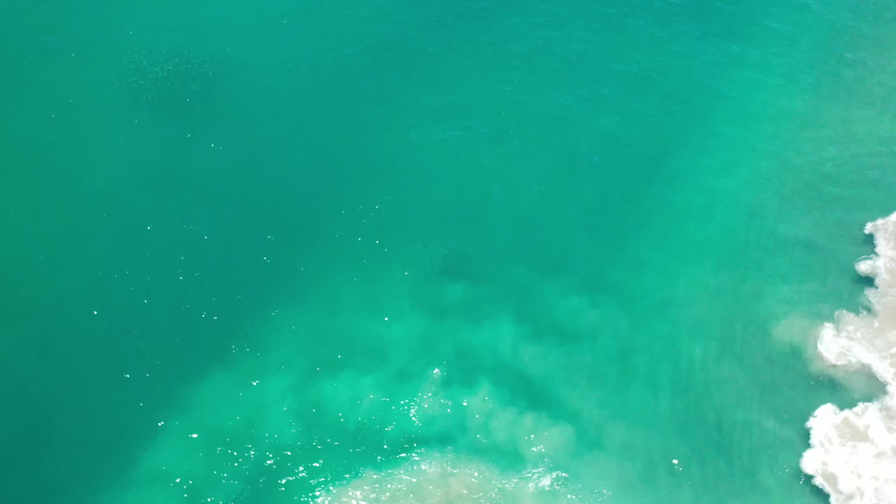 Turquoise ocean seen from above with bright foam at frame edge.