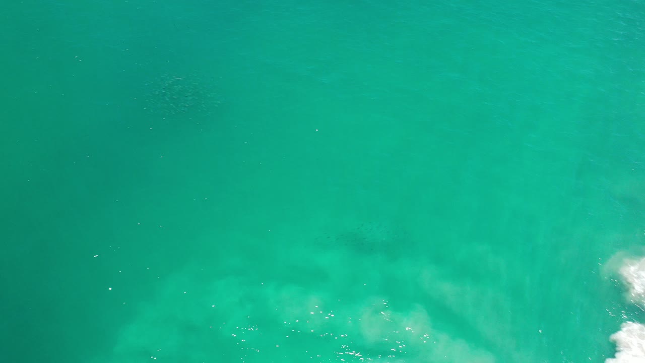 Opening frame of Los Cabos turquoise water seen from above, with a pale surf patch entering along the lower edge and no visible people.
