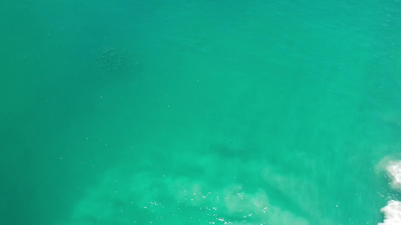 Los Cabos water fills the frame from above, with darker teal areas in the center and a brighter foamy surf edge on the right, no visible people.