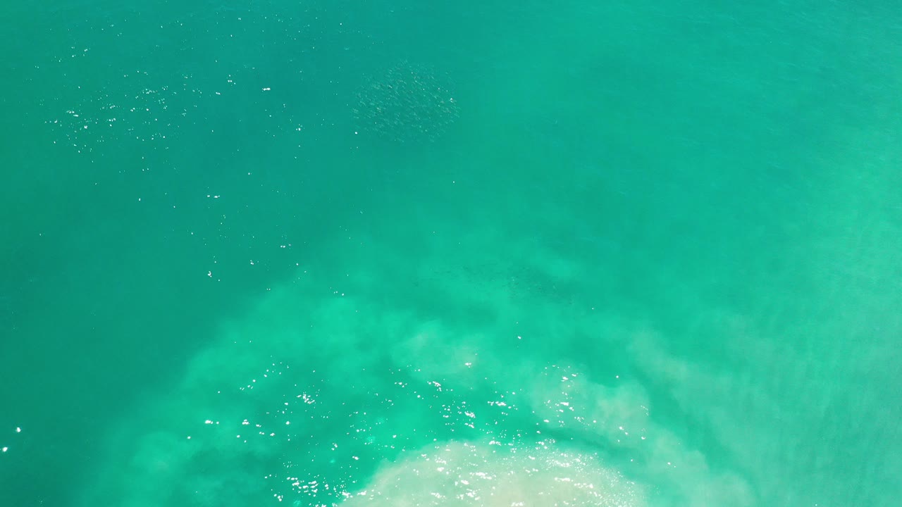 Overhead view of teal water in Los Cabos, Mexico, with pale submerged surf texture near the bottom of frame and no visible people.