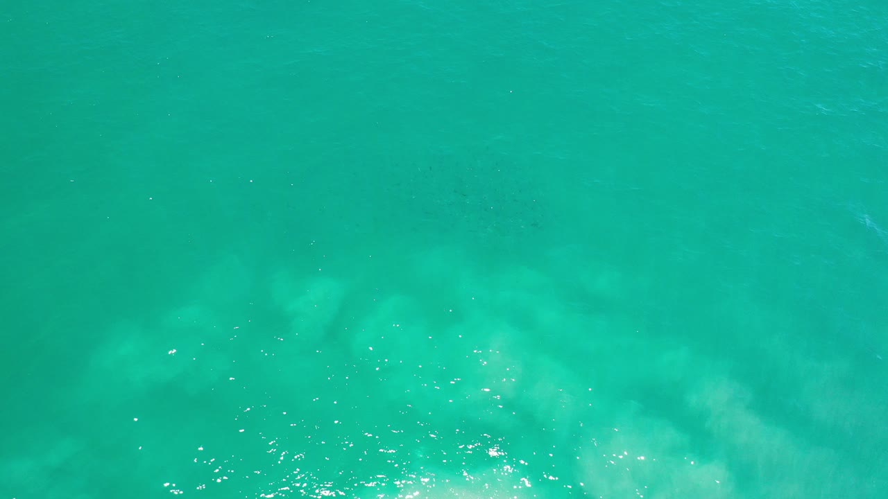 Turquoise-green ocean surface with pale underwater swirls and sun flecks.